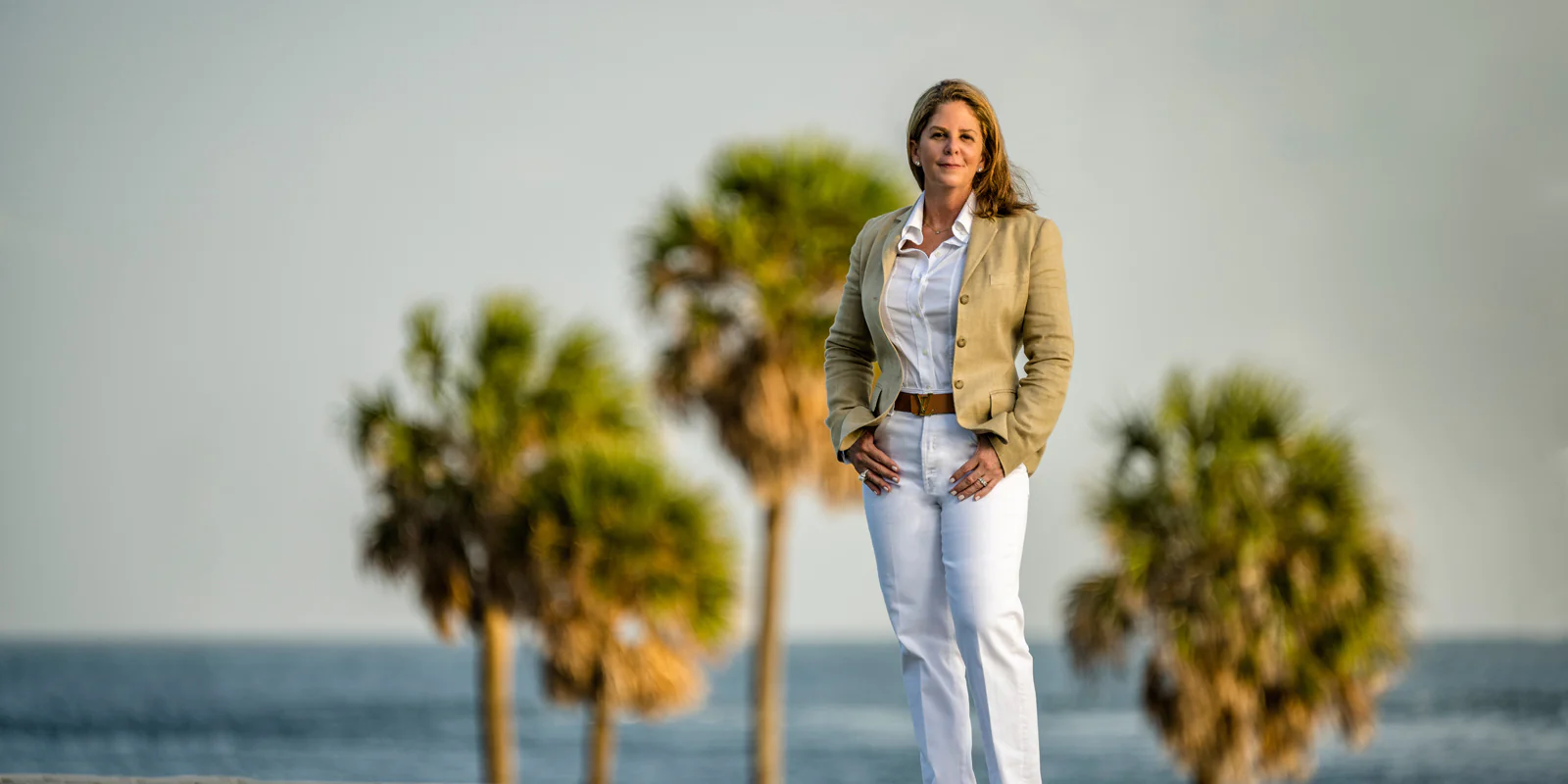 jackie joseph standing in a beige suit, with palm tree backgrounds